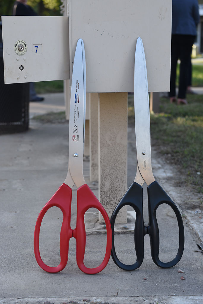Oversized scissors rest on a mailbox ahead of the ribbon-cutting